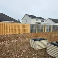 Suburban backyard with a wooden fence, leaf-covered ground, and raised garden beds under cloudy skies