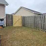 Backyard with grass, wooden fence, and a pale yellow gate between houses.