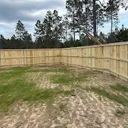 Empty fenced backyard with a wooden privacy fence and trees beyond it