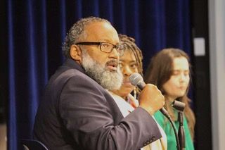 President Nimrod Chapel, Jr. speaks while panelists Dr. Cassandra Gould and ACLU Policy Director Tori Schafer look on in the background.