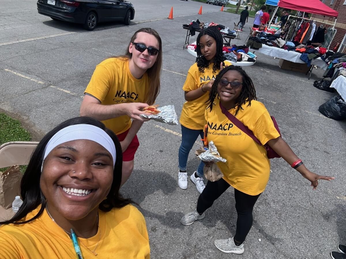 Group of SEMO students in Cape Girardeau NAACP t-shirts eating pizza at a community event in between doors.