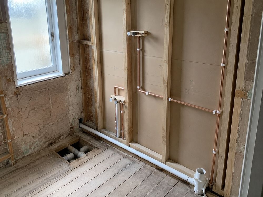 Bathroom plumbing first fix with copper pipework clipped to a stud wall and capped connections