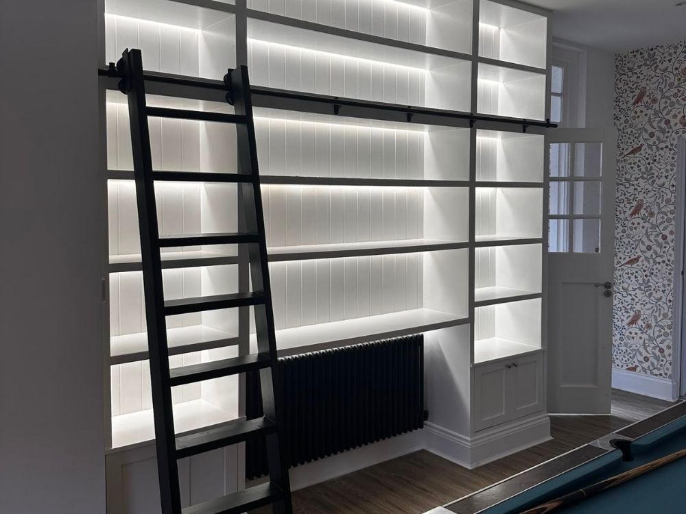 Bespoke painted library wall with LED-lit shelving, sliding ladder and integrated cupboards