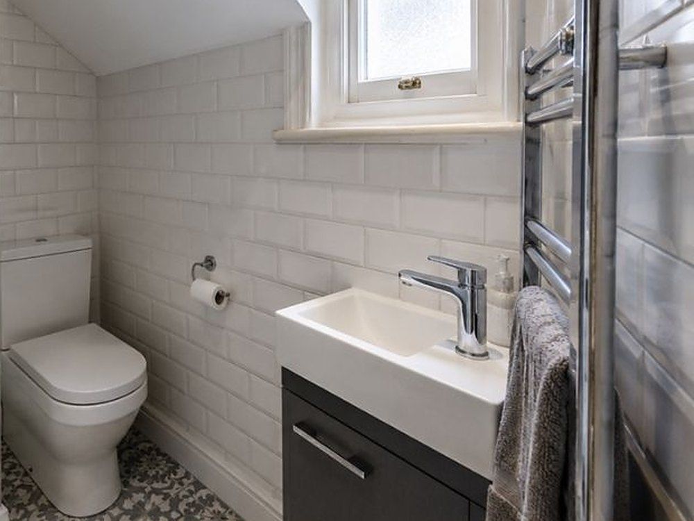 White metro wall tiles laid in a brick bond around the window and basin of a small bathroom