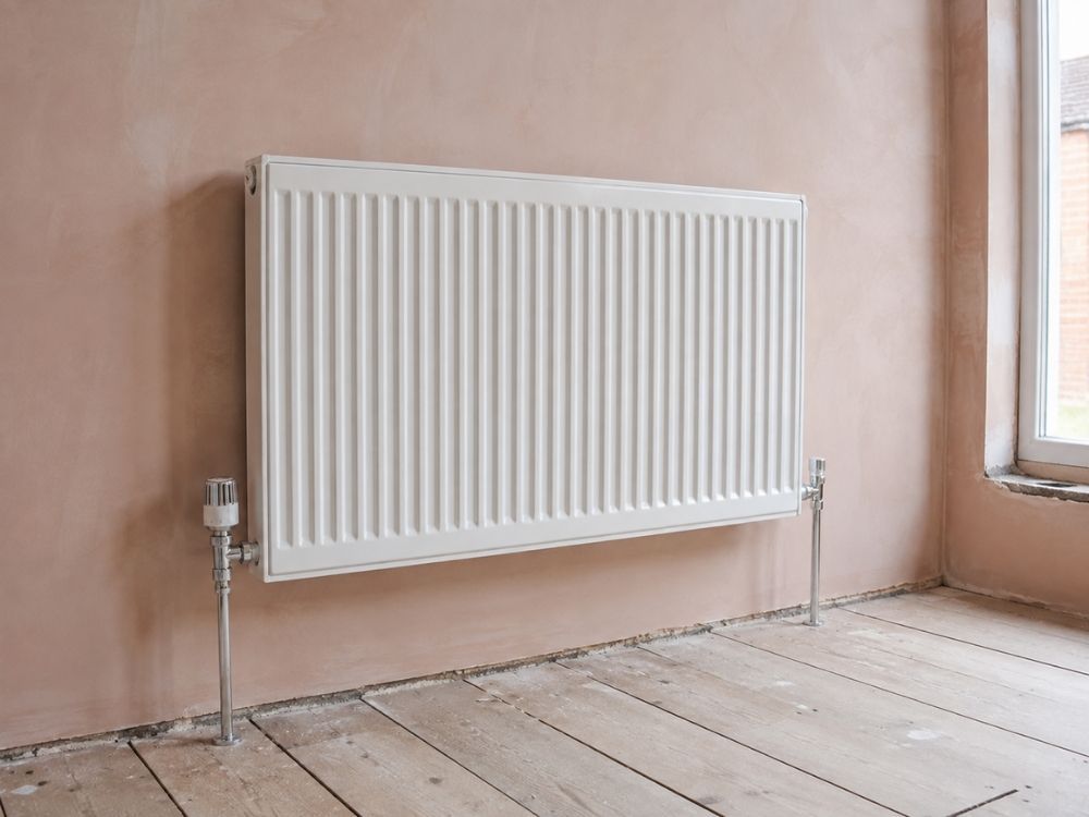 Newly fitted panel radiator with thermostatic and lockshield valves on a freshly plastered wall