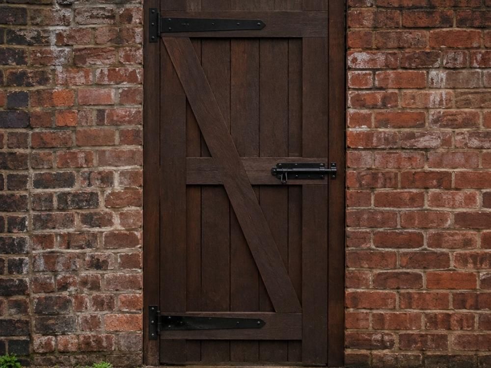 Tall boarded wooden rear entry gate set into a brick wall onto a cobbled back alley