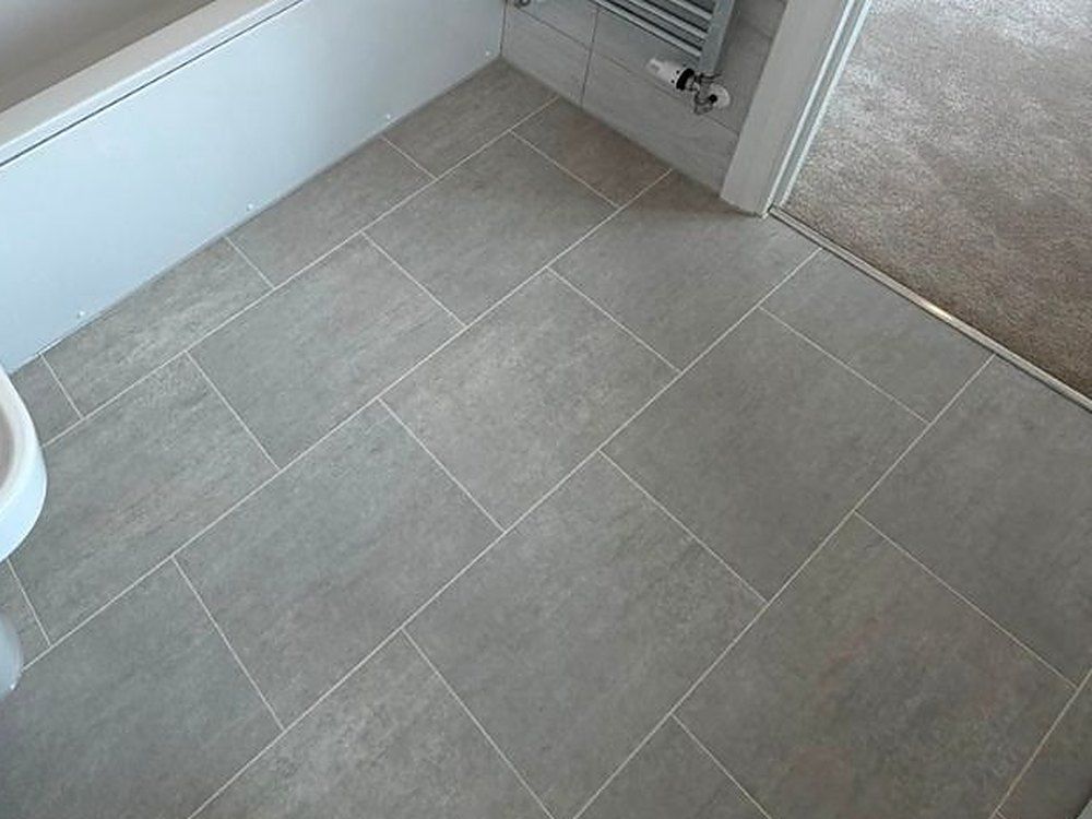 Large grey floor tiles laid in a brick pattern beside a bath and a heated towel rail