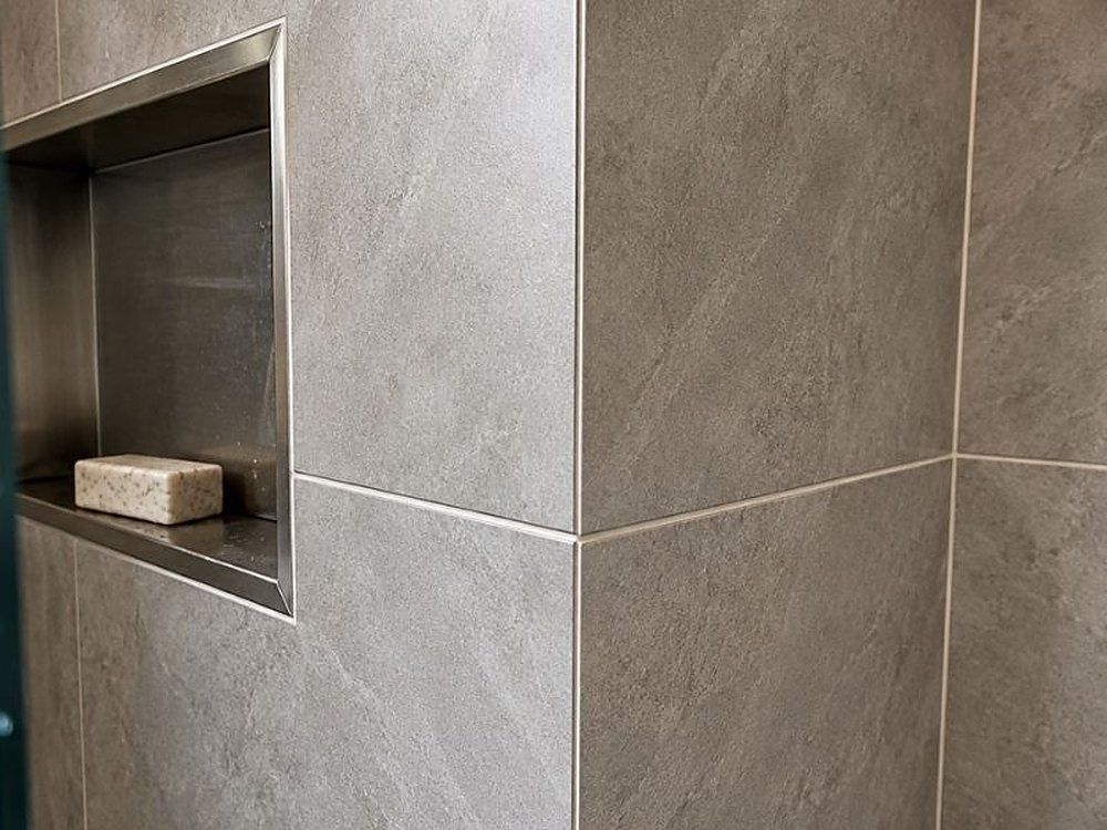Large-format grey porcelain wall tiles around a recessed shower niche with a brushed steel trim