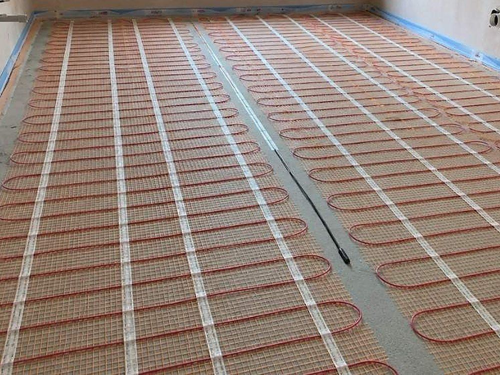 Electric underfloor heating mats laid in lanes across a primed floor, with a blue edging strip along the walls