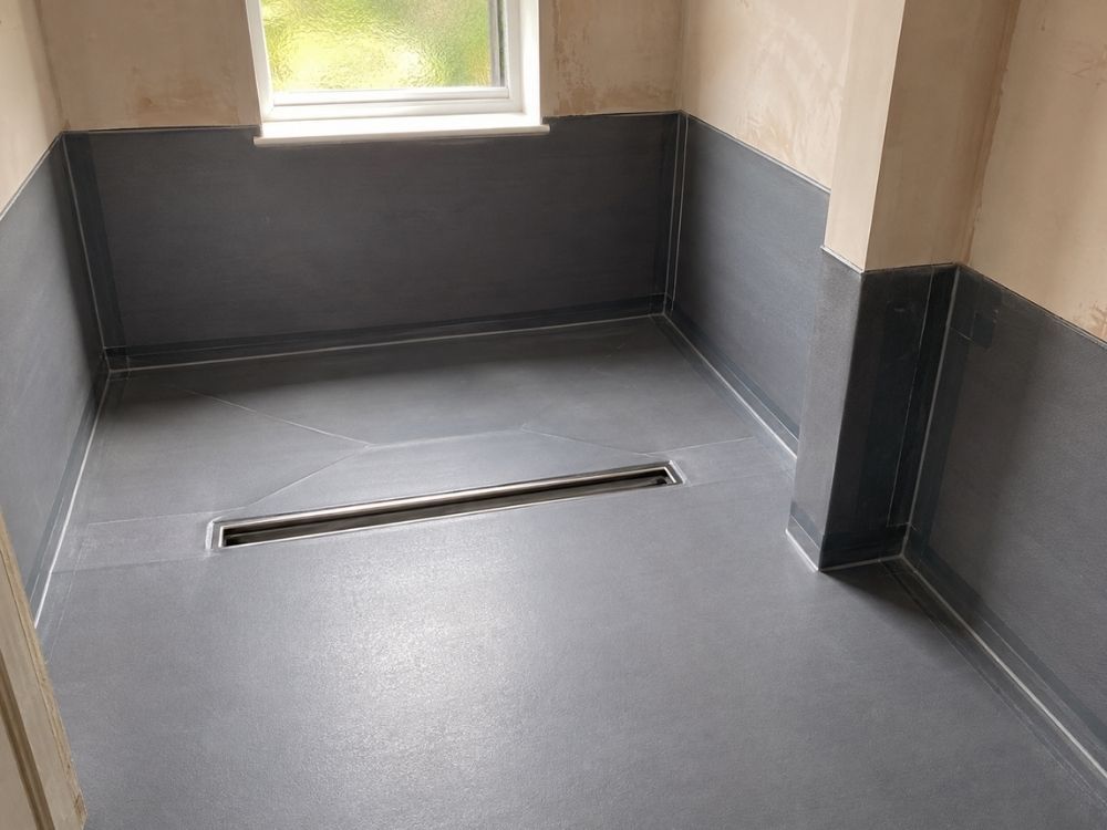 Wet room former and linear drain set into a tanked bathroom floor before tiling