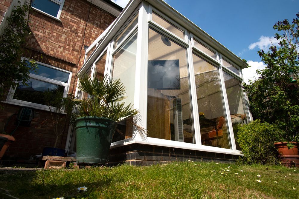 White sunroom extension with glass walls beside a brick house, set in a grassy garden — Tyrone Building Solutions in Shoal Bay, NSW