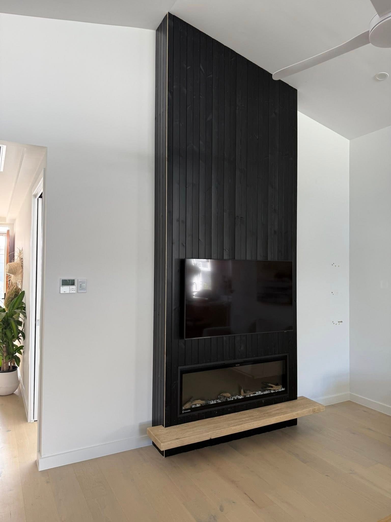 Modern fireplace with black vertical paneling and a mounted TV in a bright room — Tyrone Building Solutions in Anna Bay, NSW