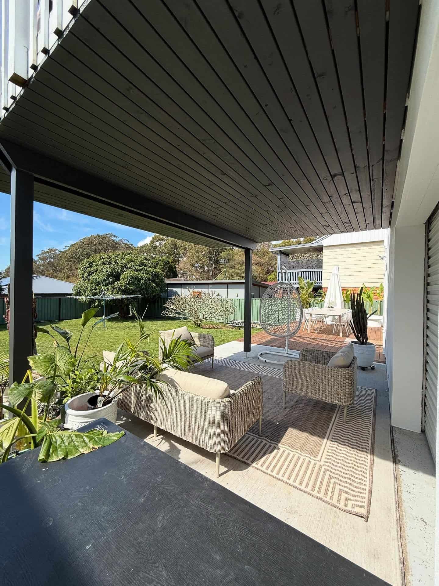 Covered patio with wicker seating, potted plants, and a view of the backyard garden — Tyrone Building Solutions in Anna Bay, NSW