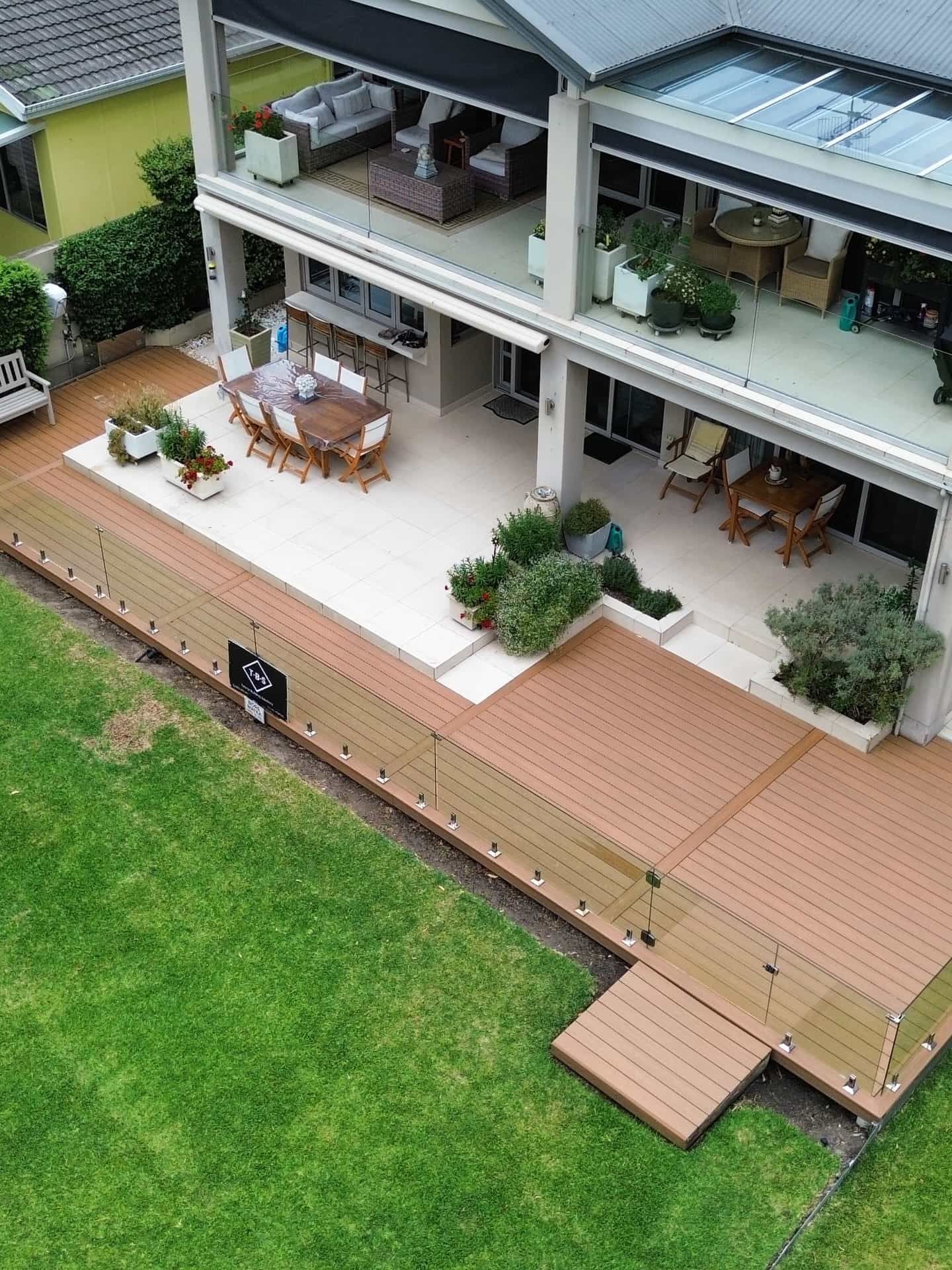 Overhead view of a covered patio with outdoor seating, potted plants, and a wooden deck beside a green lawn — Tyrone Building Solutions in Anna Bay, NSW