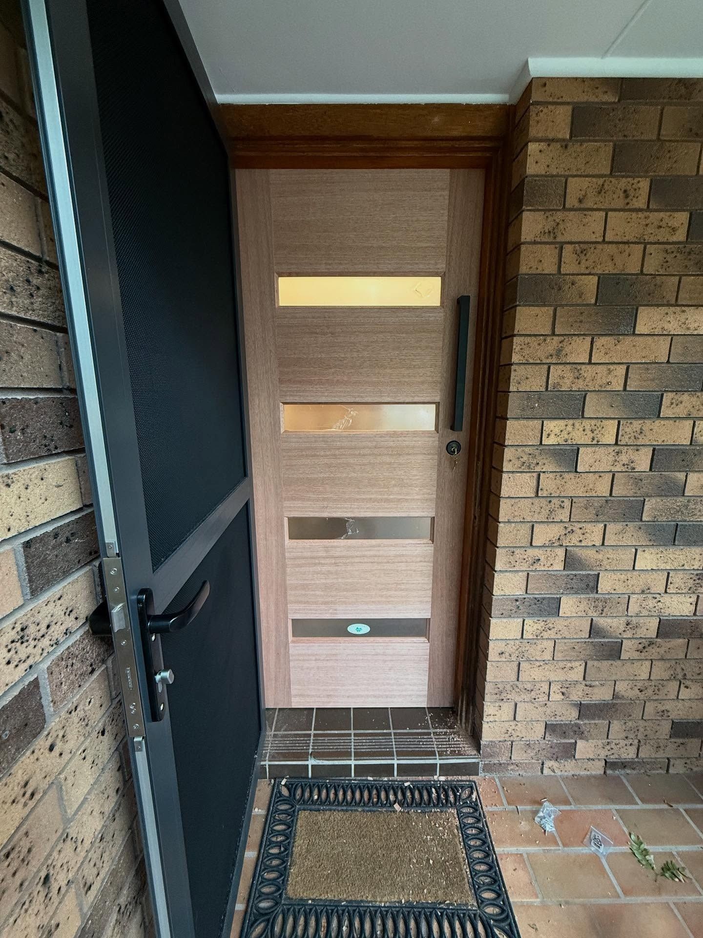 Front door with horizontal frosted glass panels beside brick walls and a doormat — Tyrone Building Solutions in Anna Bay, NSW