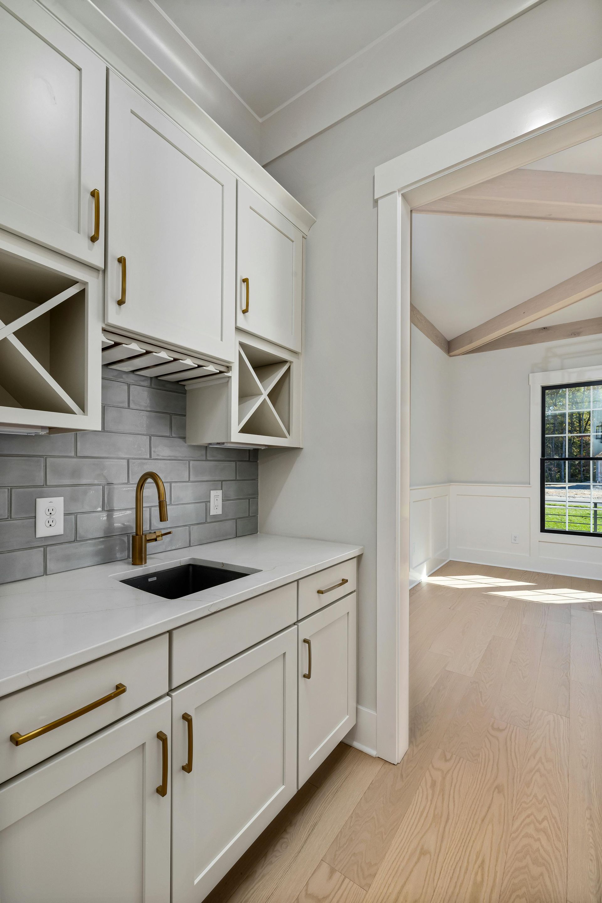 Bright white kitchen with gold fixtures, gray tile backsplash, and open doorway to a sunlit room — Tyrone Building Solutions in Anna Bay, NSW