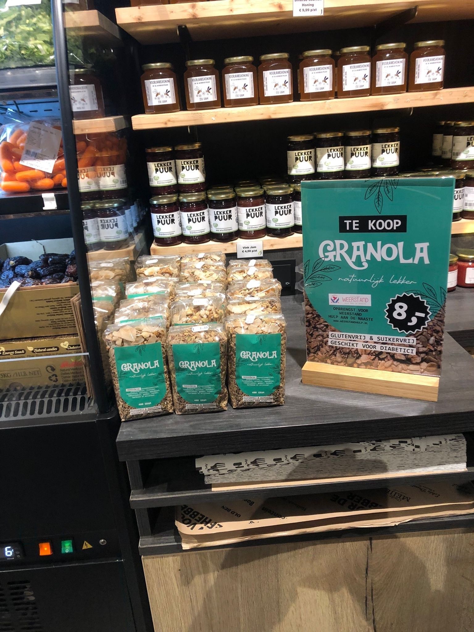 Zakken granola te koop naast een prijsbordje, uitgestald op een schap in een groente en fruitwinkel in Urk