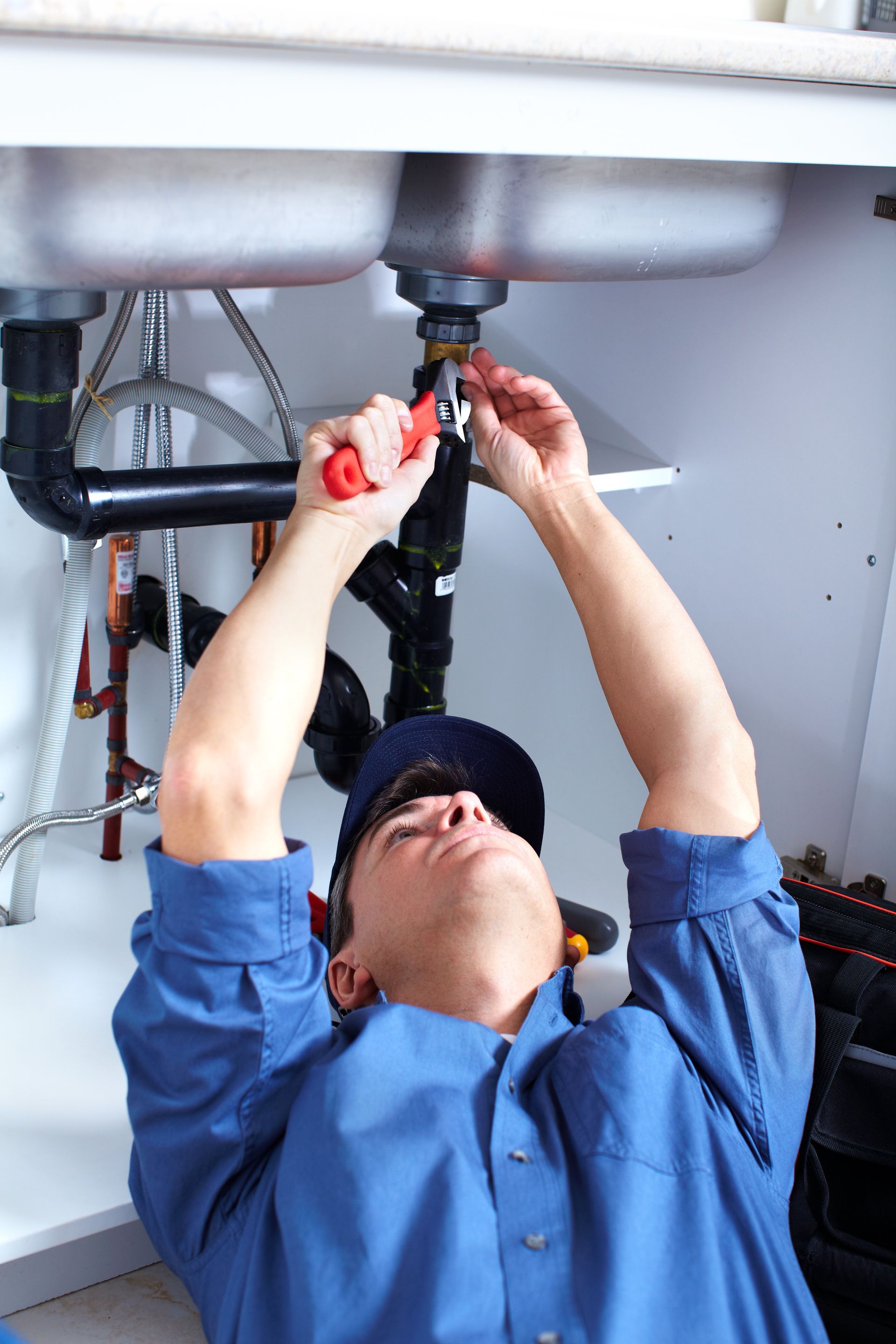 A plumber tightening pipe fittings under a sink, everyday work for residential plumbing contractors.]