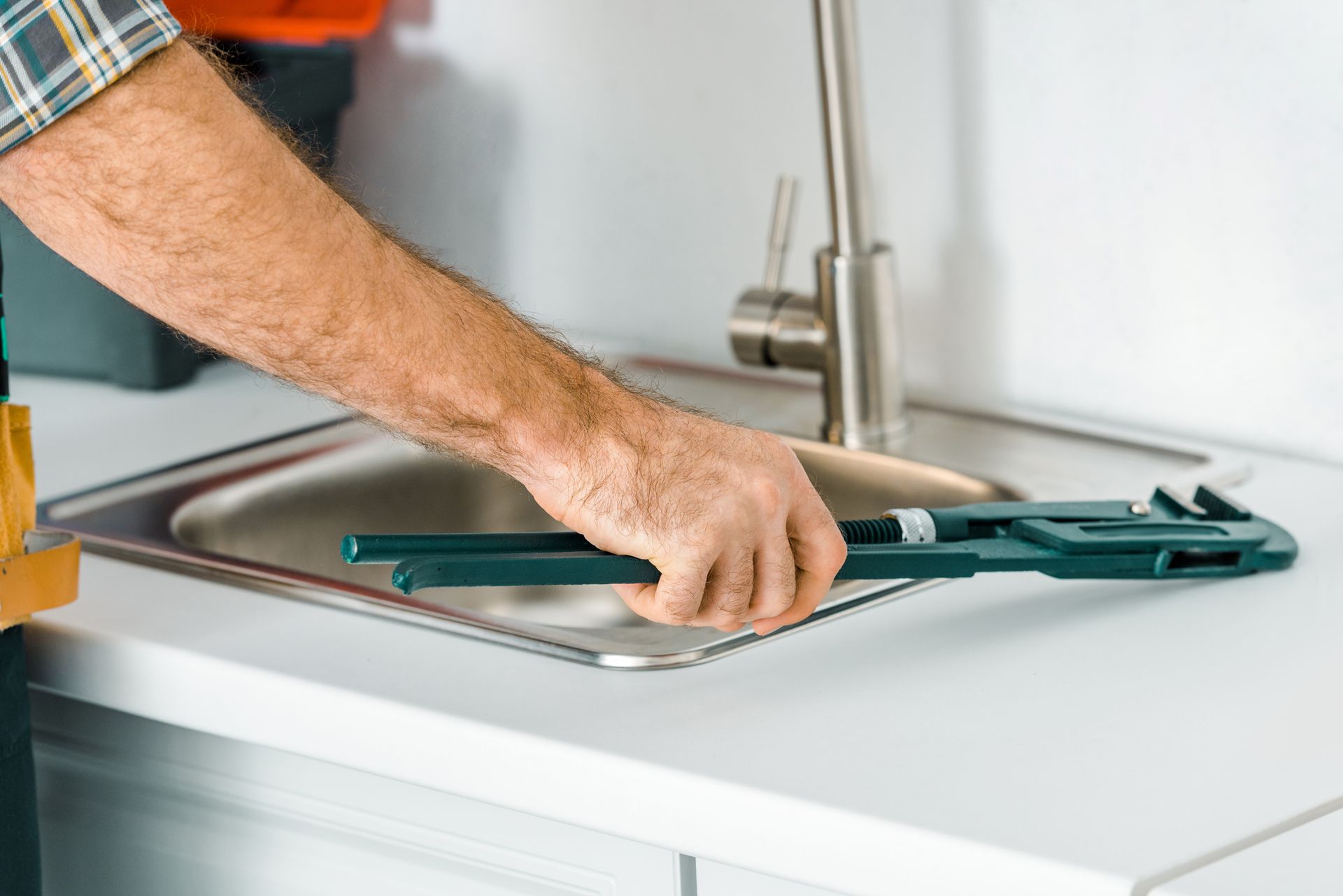 Cropped image of plumber holding monkey wrench near sink in kitchen for plumbing service Cropped image of plumber holding monkey wrench near sink in kitchen for plumbing service
