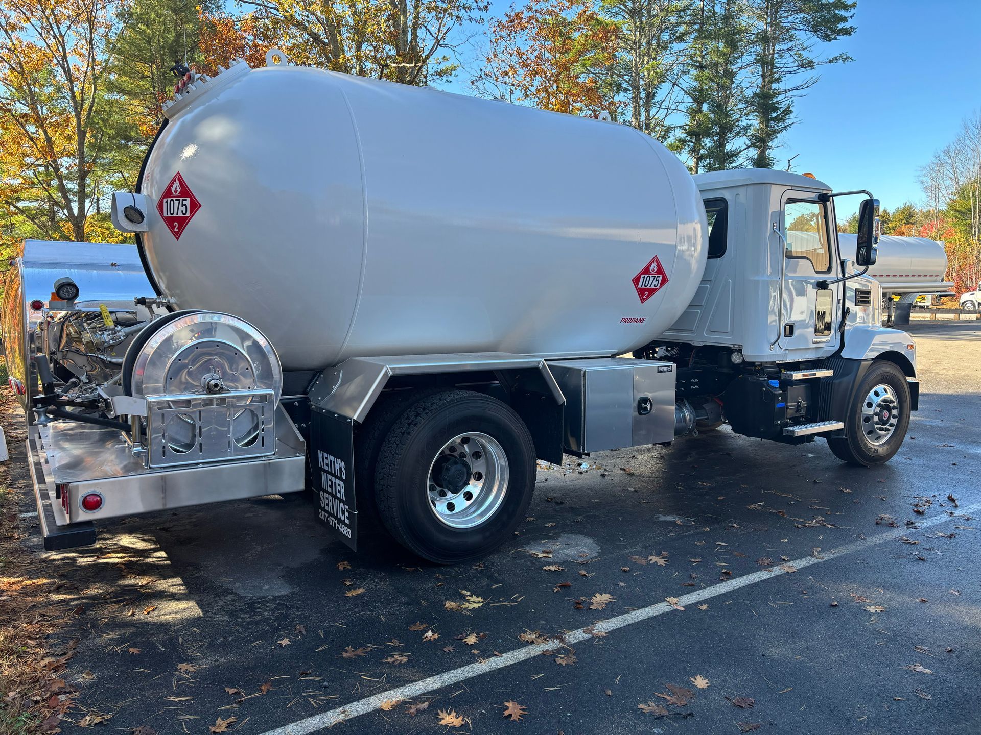 A white propane delivery truck parked on an asphalt lot with scattered autumn leaves.
