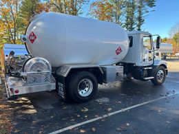 A white propane delivery truck parked on an asphalt lot with scattered autumn leaves.