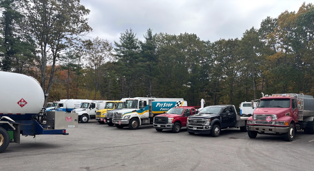 A parking lot filled with various commercial tanker and pickup trucks parked in front of a wooded area.