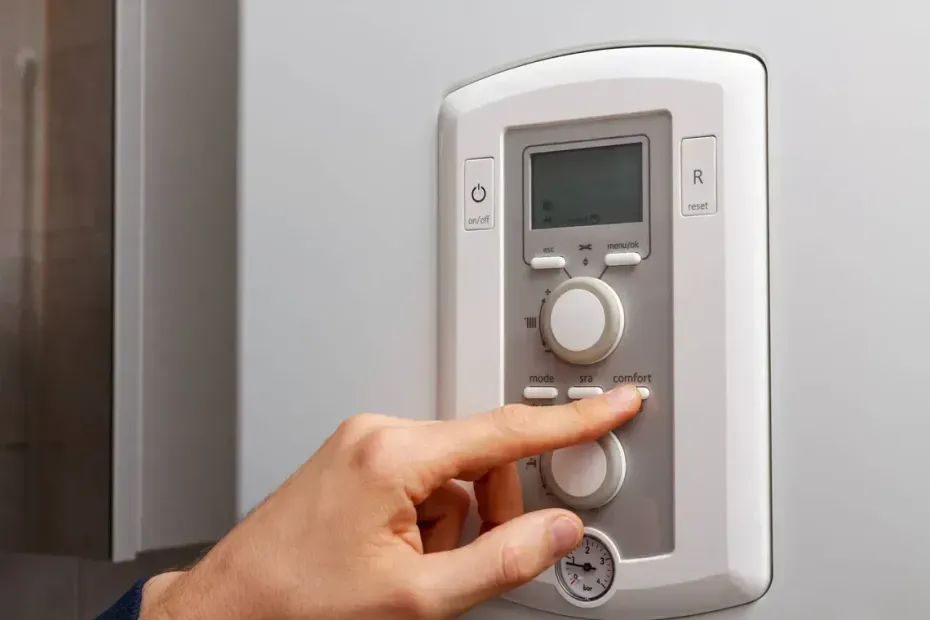 Una mano preme un pulsante rotondo su un termostato bianco a parete con un piccolo display.