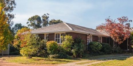 A large brick house surrounded by trees and bushes on a sunny day.