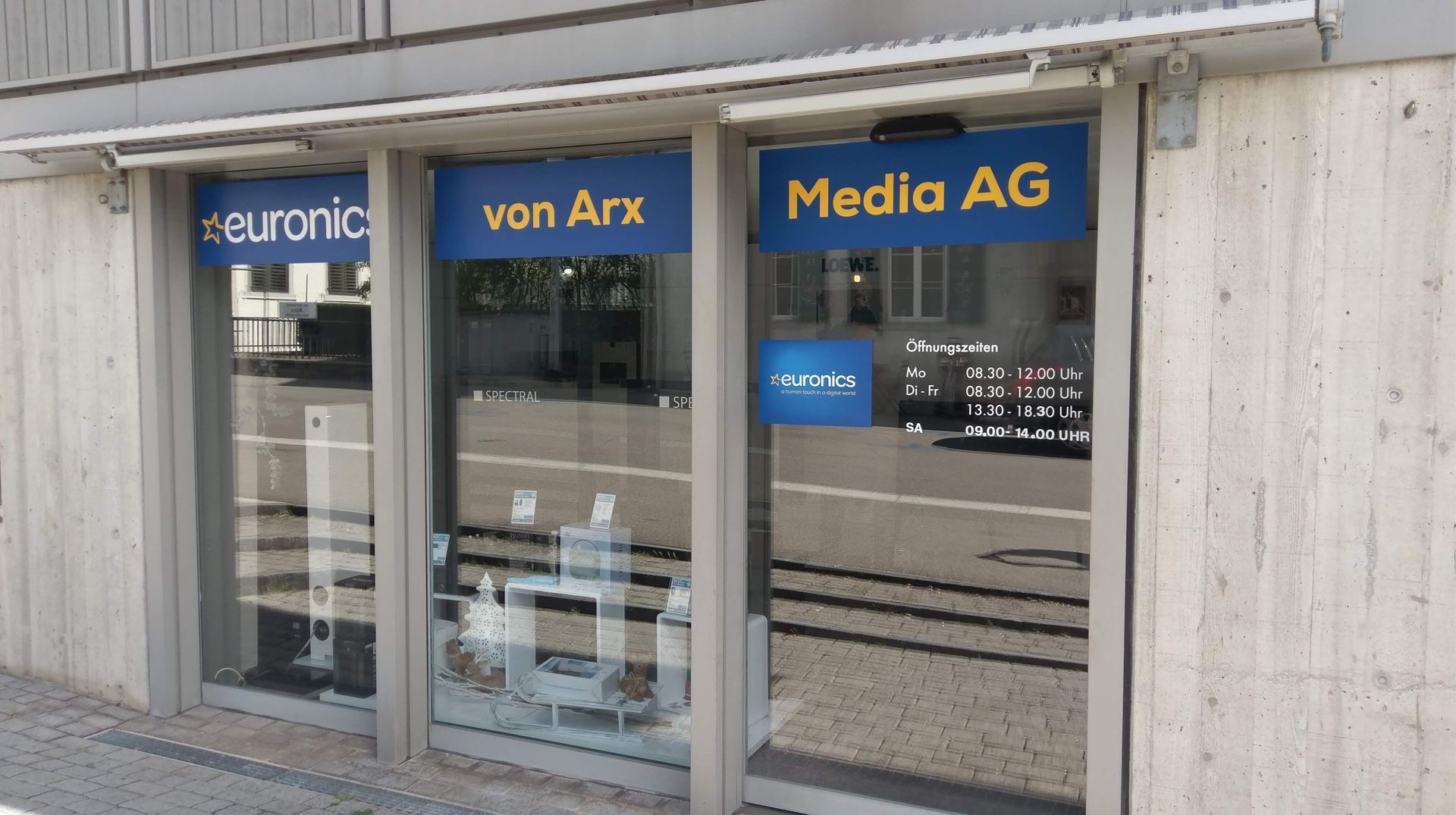 Schaufenster mit Glastüren und blauen Schildern mit der Aufschrift „euronic“, „von Arx“ und „Media AG“