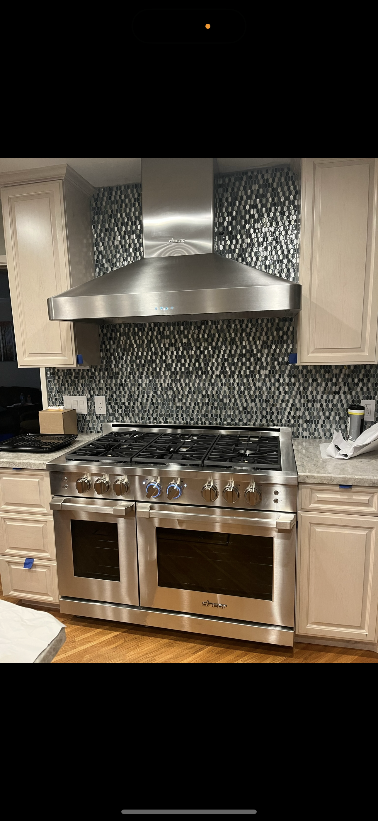 A stainless steel gas stove and range hood set against a black and white patterned mosaic tile backsplash.