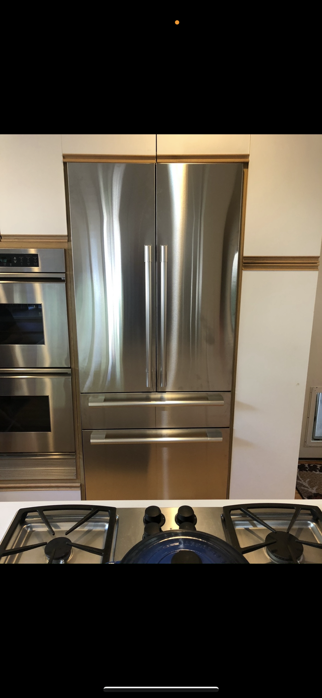 A stainless steel French door refrigerator set into a kitchen wall, adjacent to a double wall oven and kitchen stovetop.