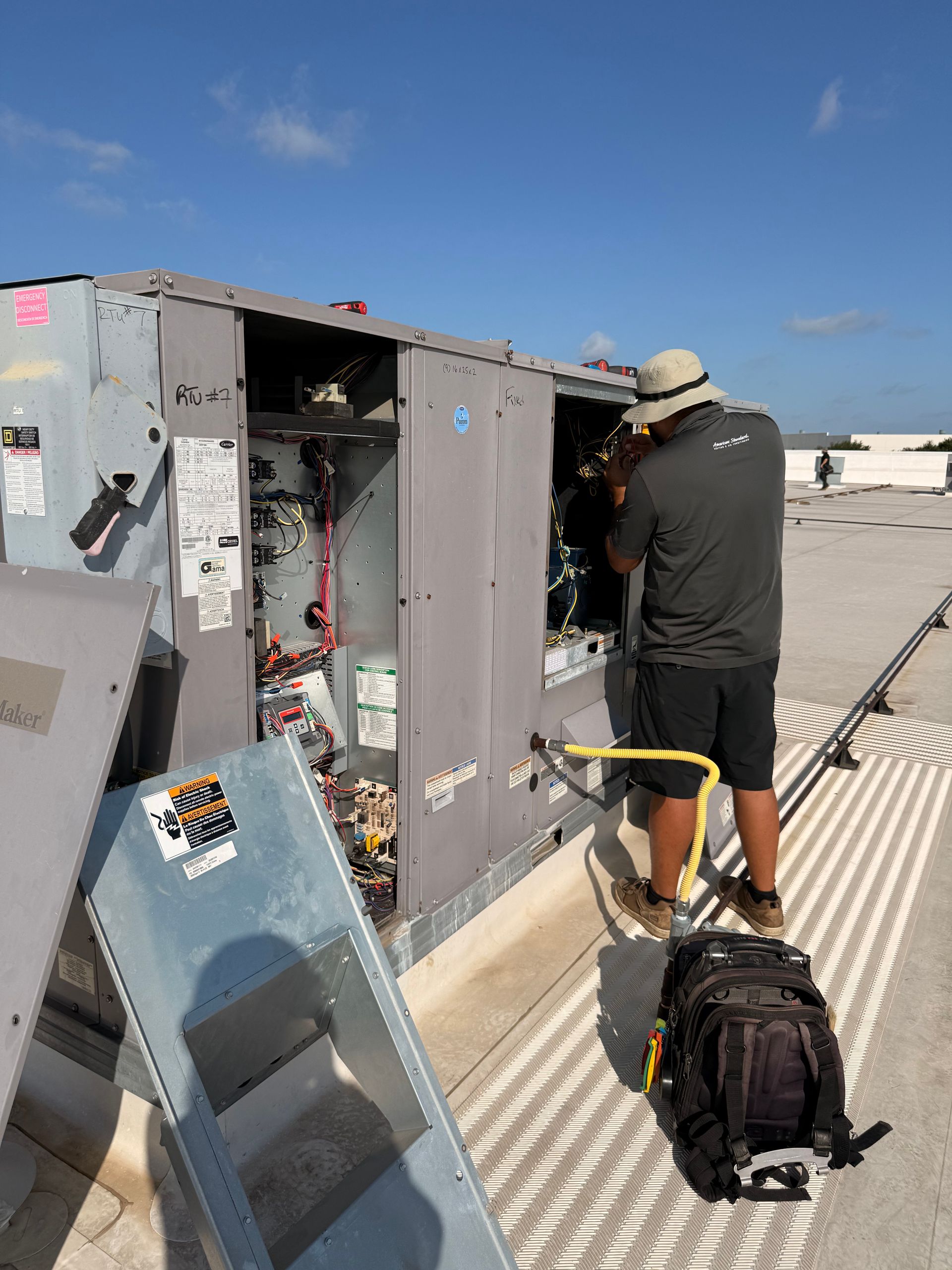 Worker inspecting rooftop electrical equipment beside an open gray cabinet on a sunny day