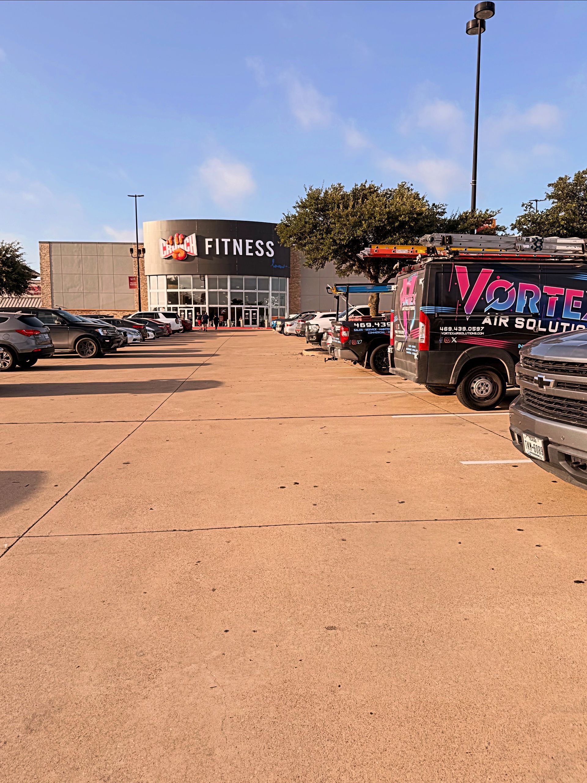 Parking lot leading to a Crunch Fitness storefront with parked cars on both sides