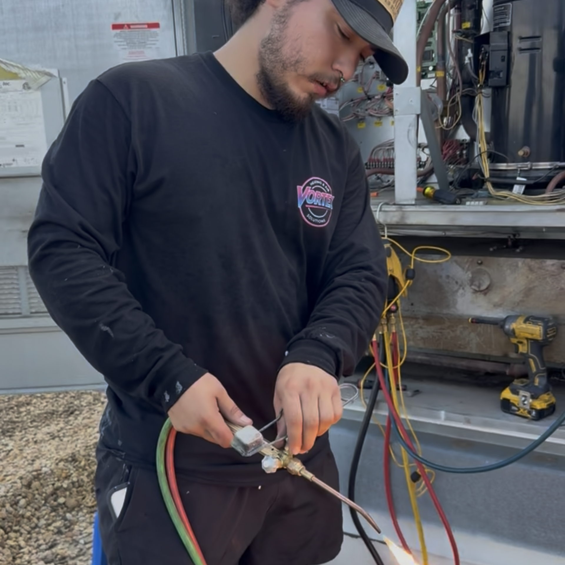 Worker in black shirt adjusts hoses on industrial equipment outdoors.