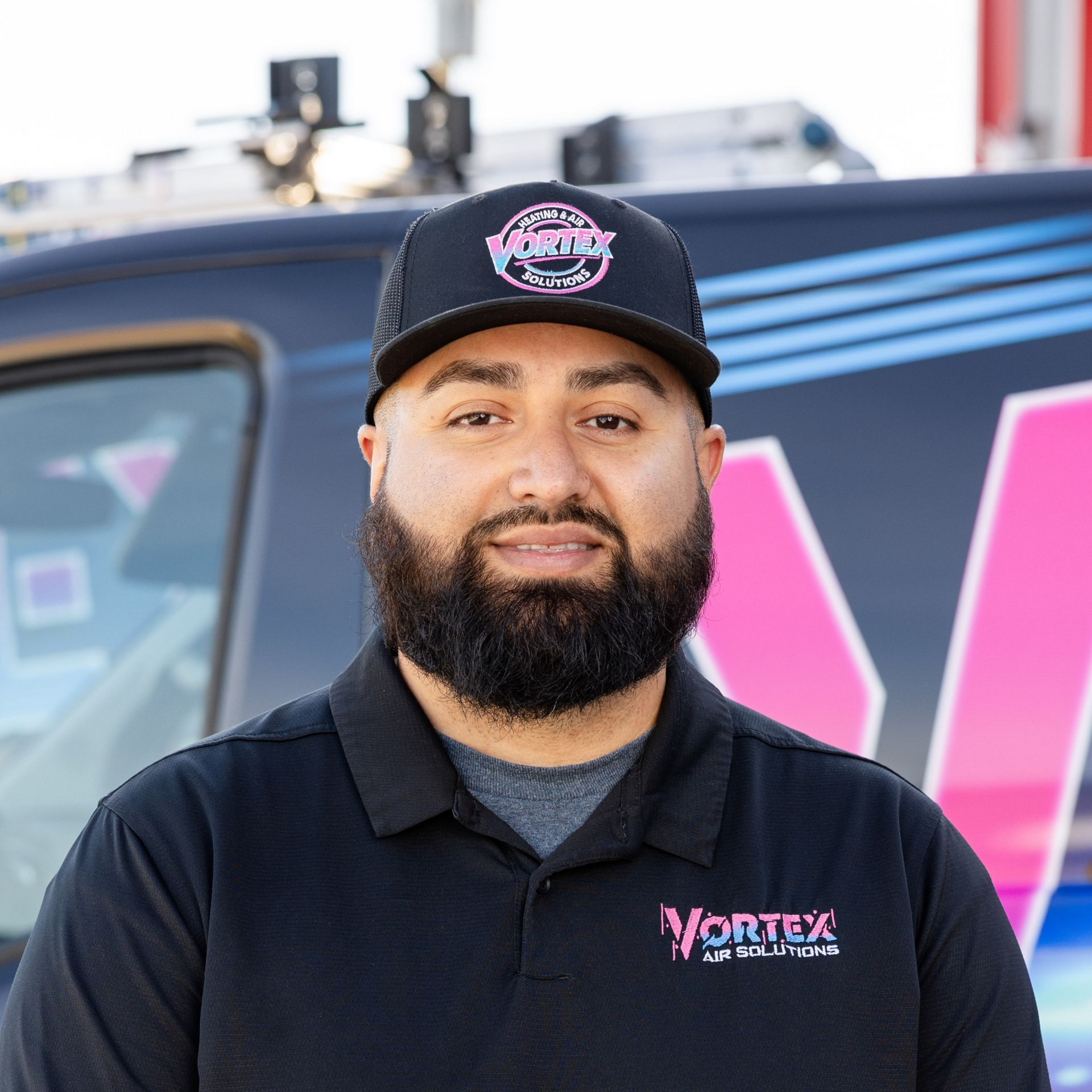 Man with dark hair and beard, wearing a navy polo shirt, smiles at the camera.