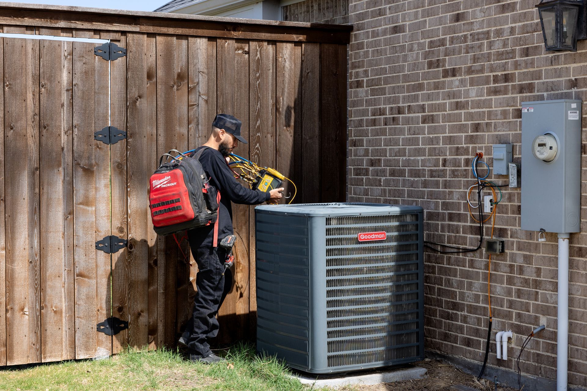 Two gray air conditioning units sitting on a brick patio next to a house.