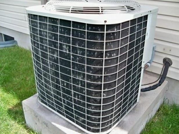 Outdoor central air conditioner unit on a concrete pad beside a house with siding and grass.