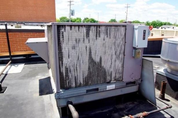 Dirty rooftop HVAC unit with a weathered metal grille and adjacent ductwork