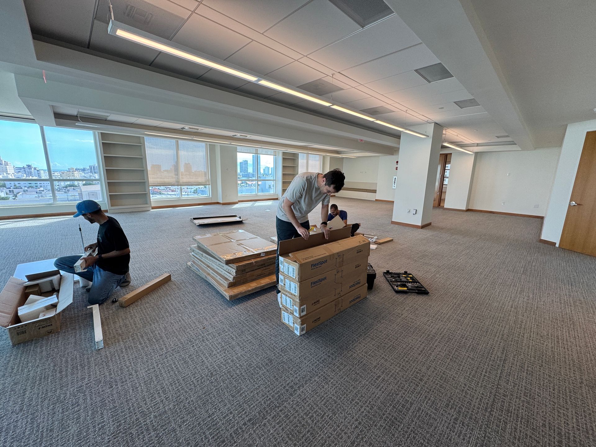 Two men are working on a wooden floor in an empty room.