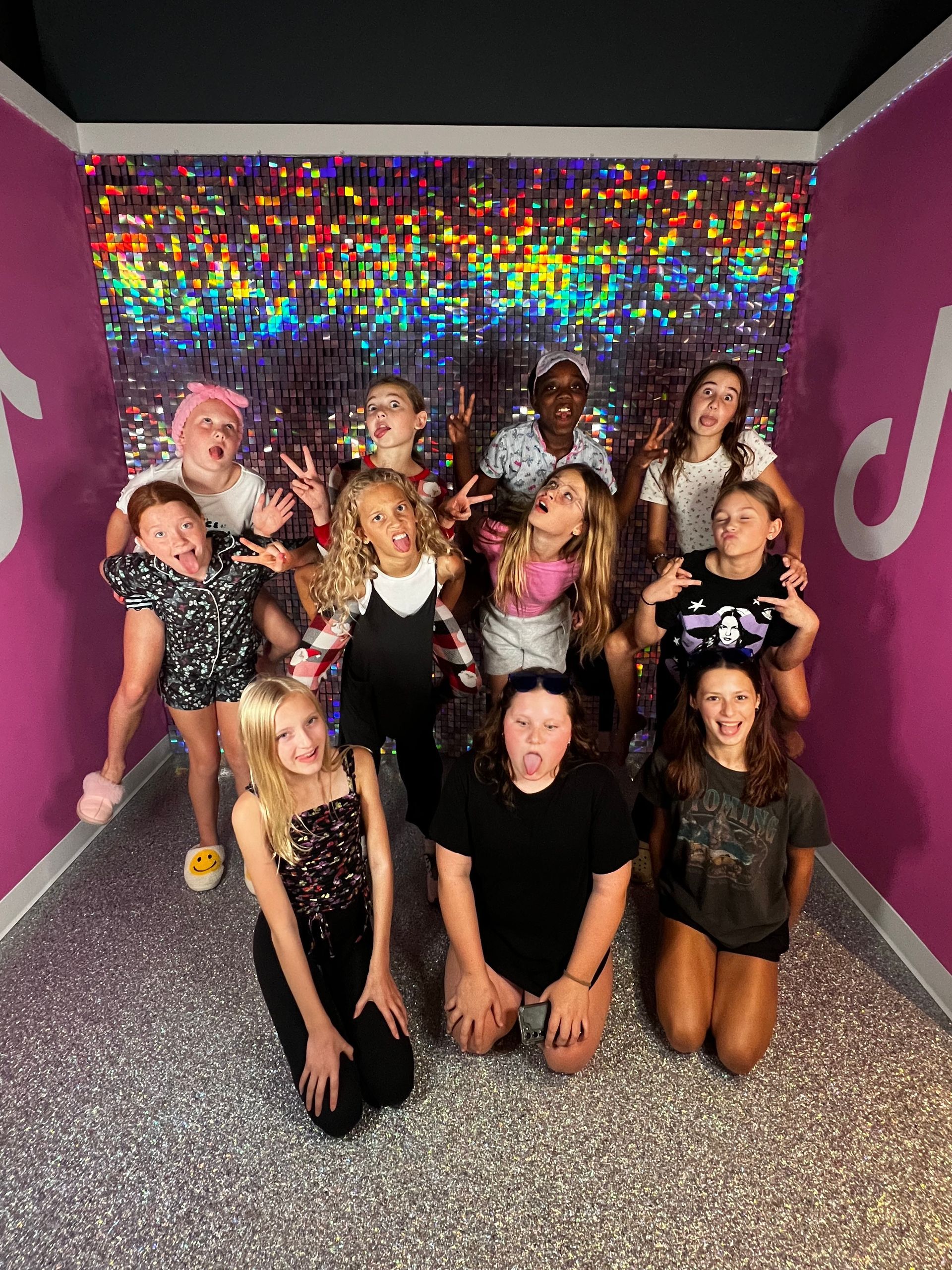 Group posed in a glittery hallway with colorful wall lights and purple sides, smiling at the camera.