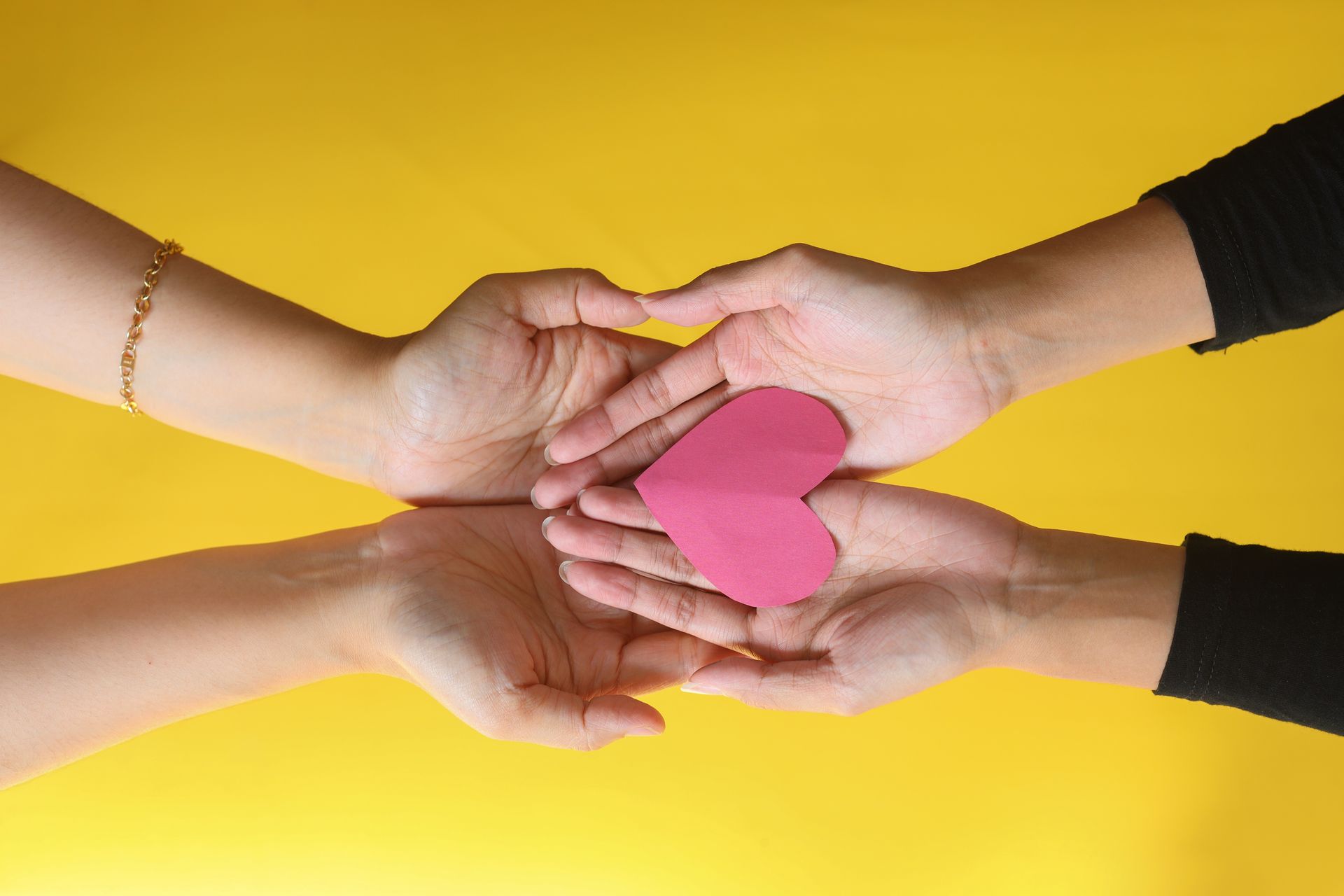 Two people are holding a pink heart in their hands.