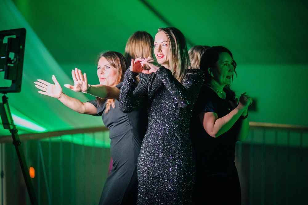 Three performers in black dresses dancing on a green-lit stage