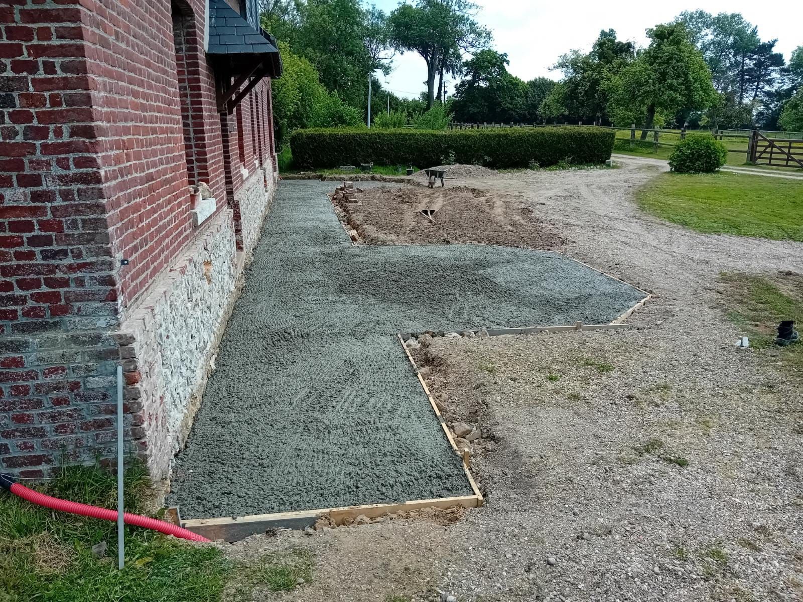Maison en briques avec des dalles de béton frais le long d'un chemin de gravier et d'une haie de jardin.