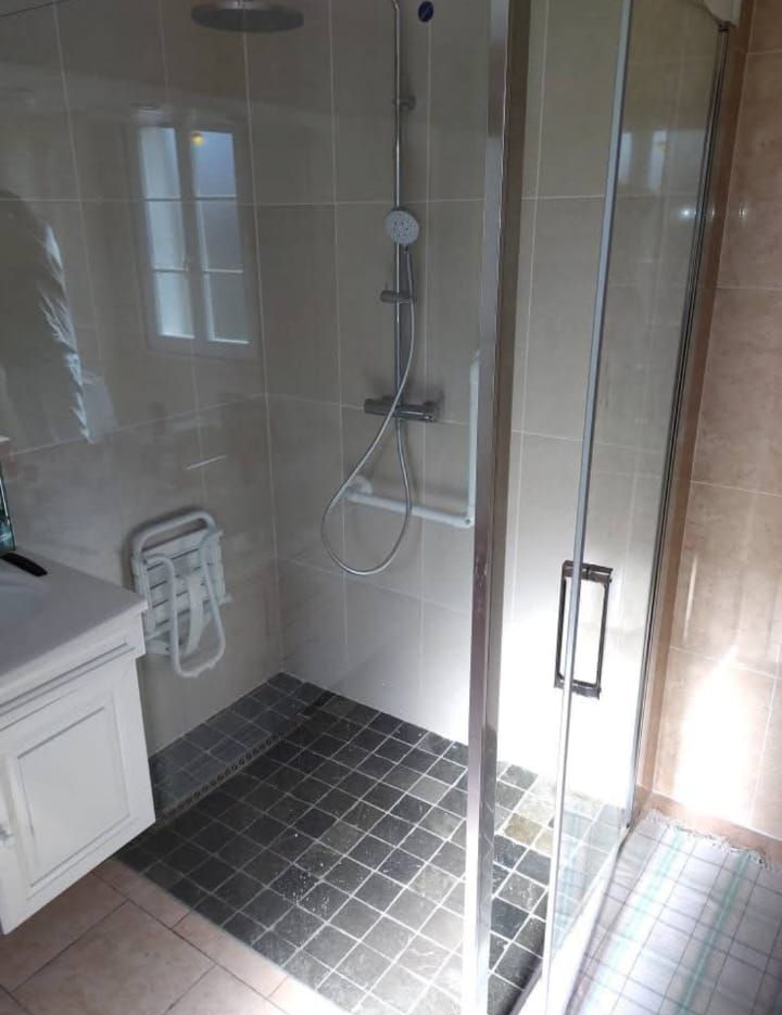 Salle de douche moderne avec porte en verre, sol carrelé gris et lavabo blanc.