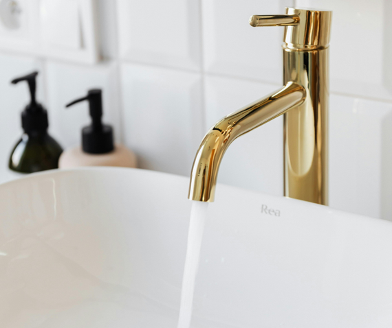 Gold faucet pouring water into a white sink, soap dispensers in the background.