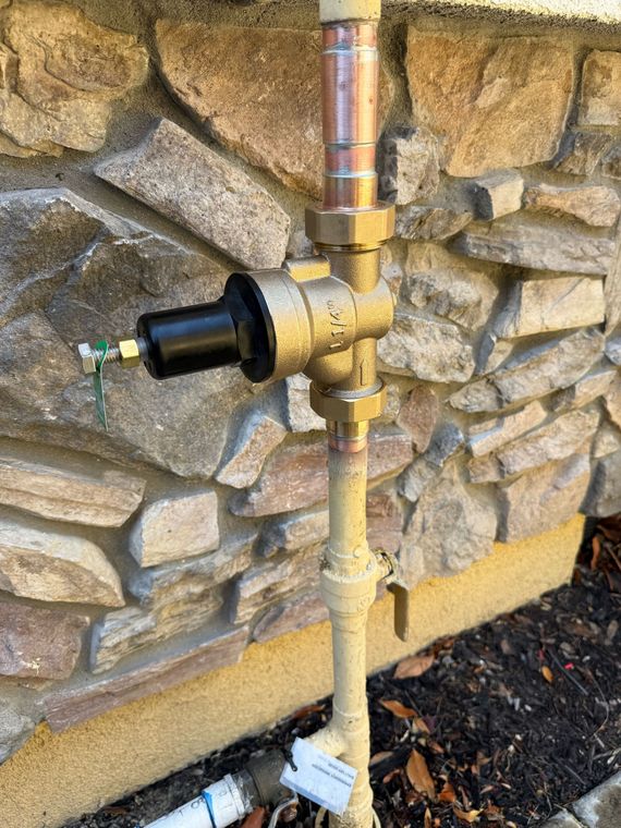 Silver pressure relief valve connected to gray pipes with black fittings.