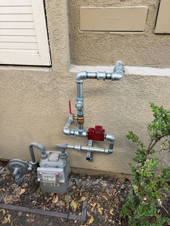 Person using a yellow gas leak detector on copper pipes in a utility room.