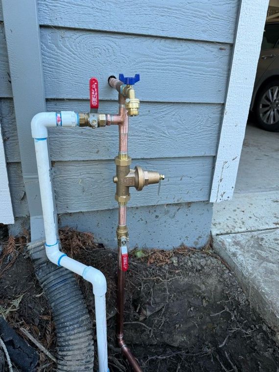 A blue water pipe sprays water; it is broken, in a ditch. Concrete pipe is visible.