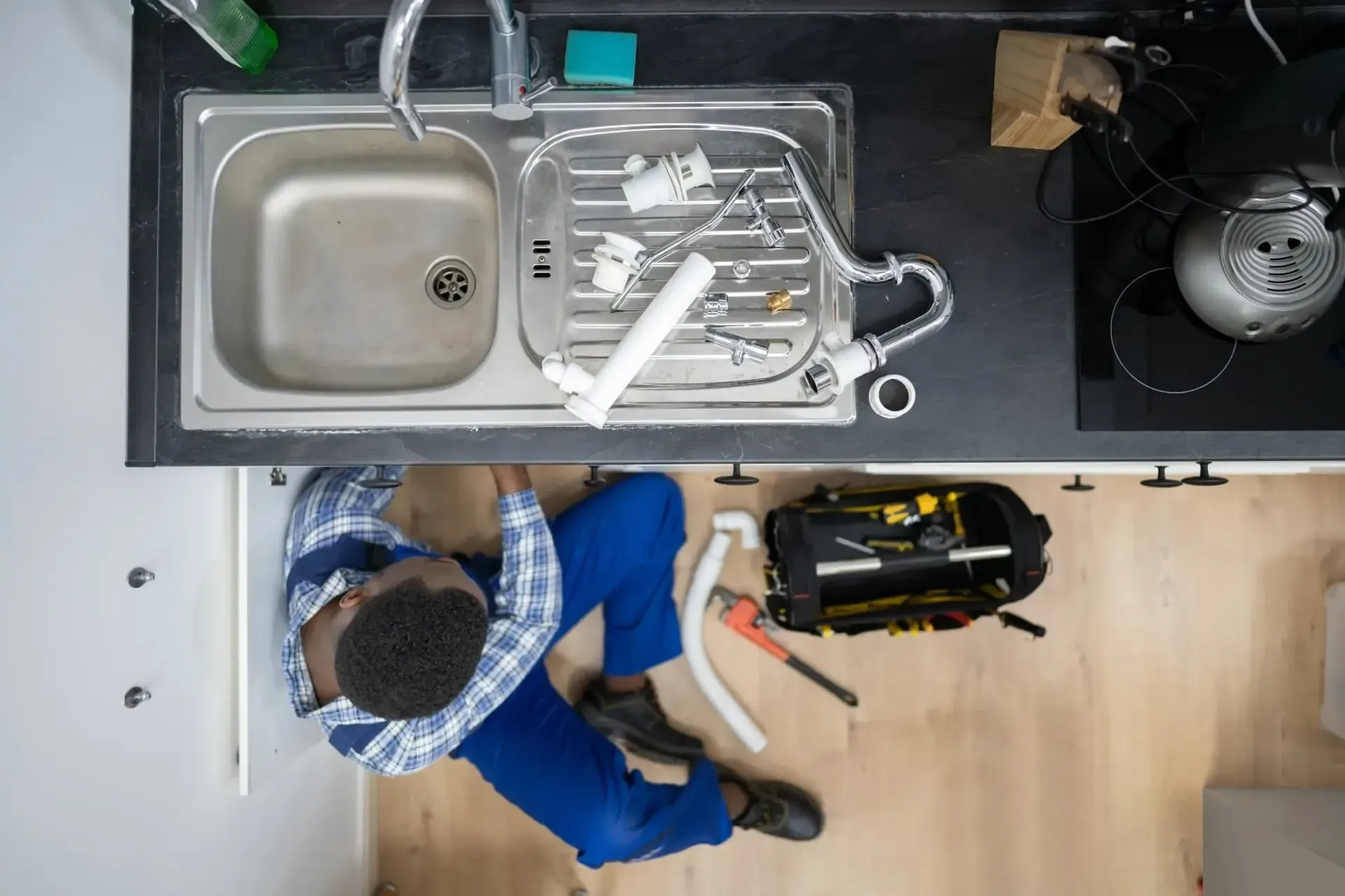 Plumber working under a kitchen sink, surrounded by tools and pipes.