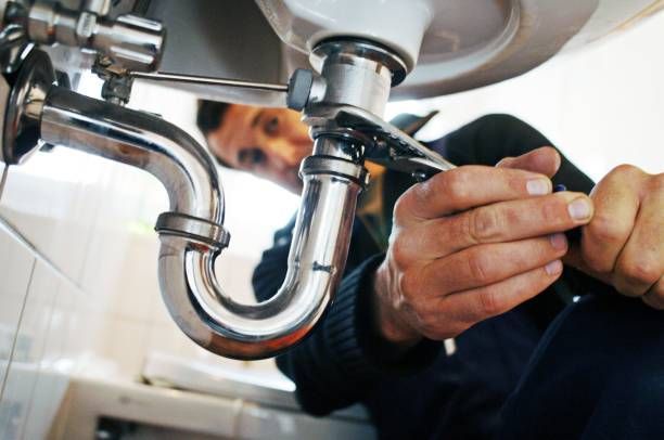 Plumber working on sink pipes with a wrench, likely repairing a drain.